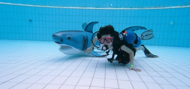 Kind mit Taucherausrüstung und einem Kunststoffhai unter Wasser