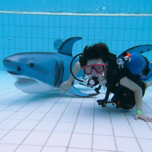 Kind mit Taucherausrüstung und einem Kunststoffhai unter Wasser