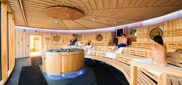 Personen in einer großen Sauna mit Aufgussofen im Zentrum