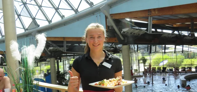 Mitarbeiterin bringt essen im Gastronomiebereich mit Blick auf das Erlebnisbecken