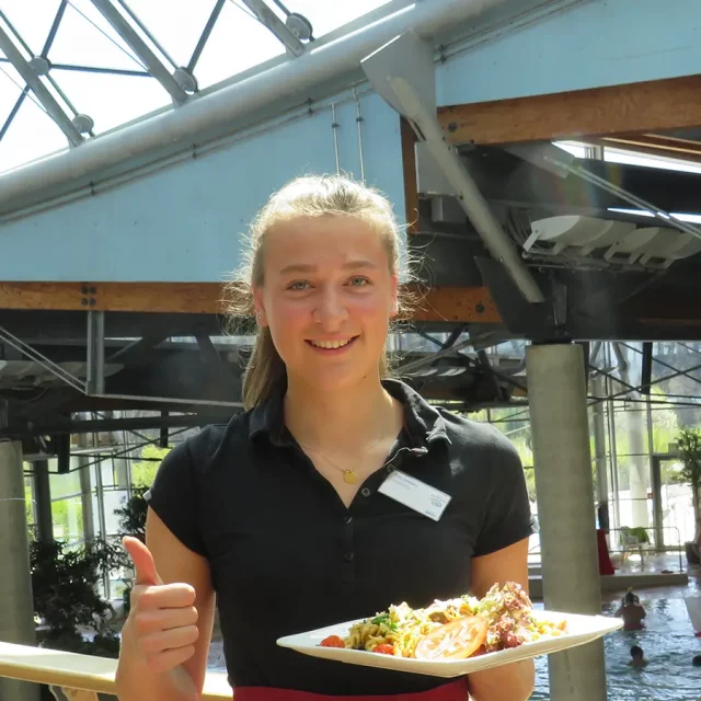 Mitarbeiterin bringt essen im Gastronomiebereich mit Blick auf das Erlebnisbecken